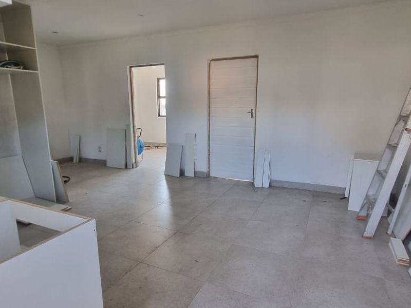 An open-plan living and kitchen area currently undergoing renovation, featuring tiled floors and partially installed cabinetry.