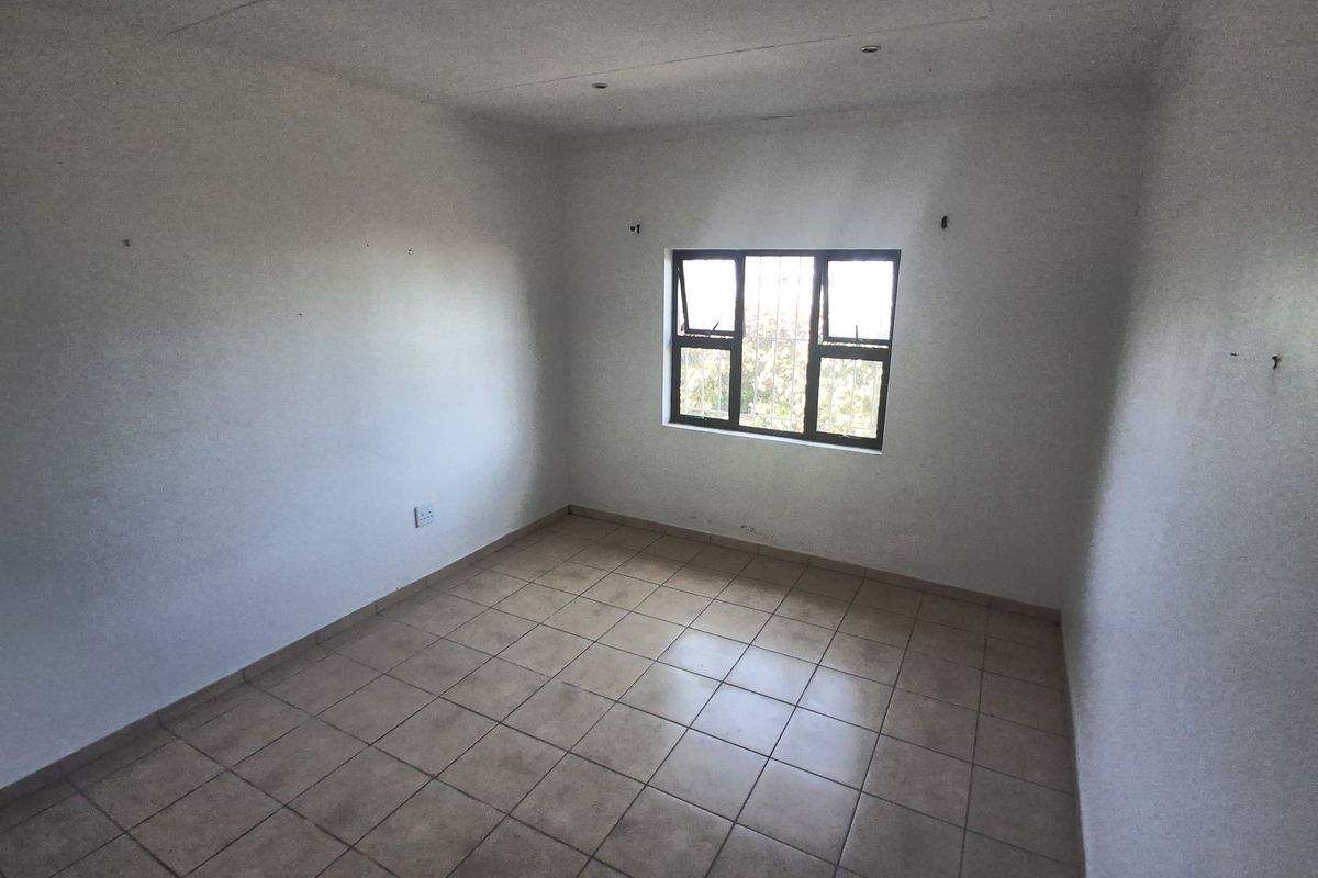 An empty bedroom featuring tiled flooring, recessed ceiling lights, and a window fitted with security bars.