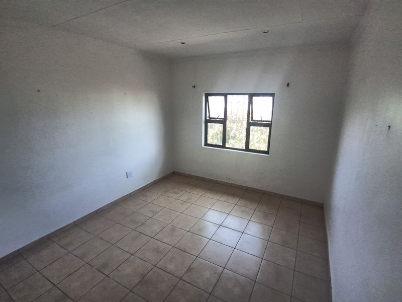 An empty bedroom featuring tiled flooring, recessed ceiling lights, and a window fitted with security bars.