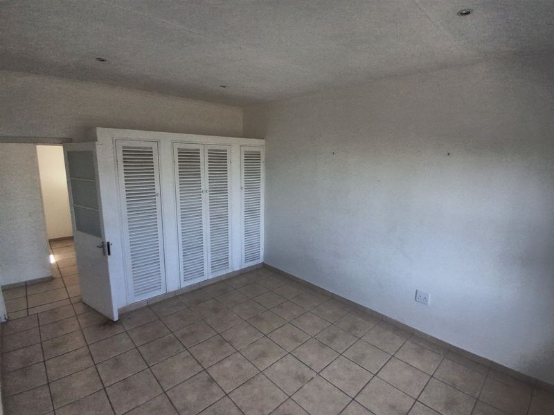 An empty bedroom featuring tiled flooring, recessed downlighting, and white louvered built-in cupboards, offering a blank canvas for personalization.