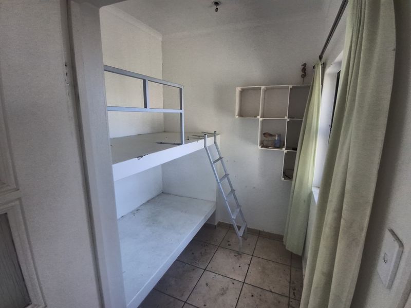 Small bedroom featuring a built-in bunk bed, wall-mounted shelving, and tiled flooring. The space requires cosmetic updates and maintenance.