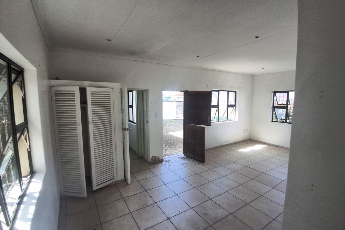An empty living area featuring tiled flooring, built-in cupboard storage, and aluminium window frames, leading out to an exterior paved area.