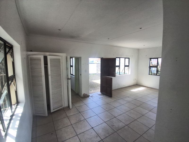 An empty living area featuring tiled flooring, built-in cupboard storage, and aluminium window frames, leading out to an exterior paved area.