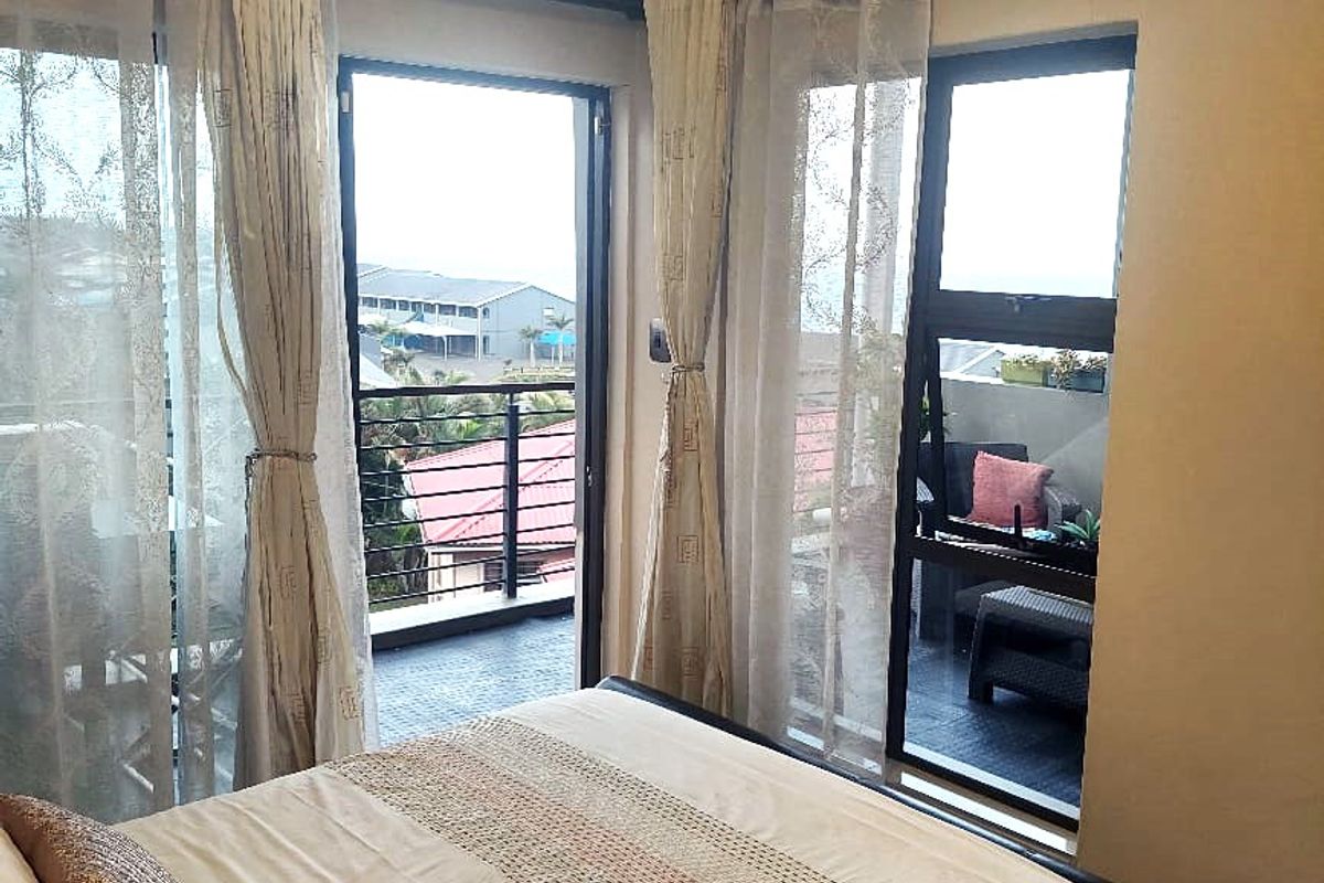 A bright bedroom featuring large glass sliding doors that open onto a private balcony, providing natural light and outdoor access.