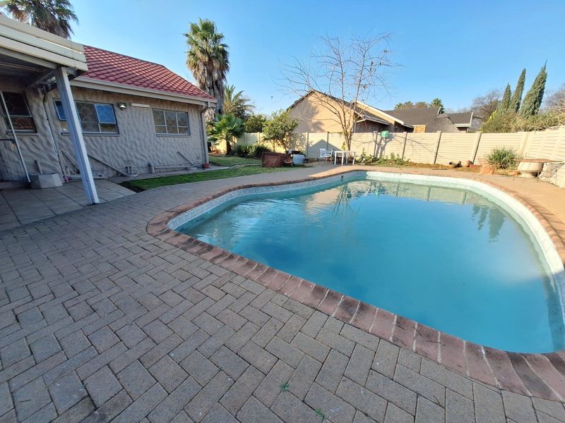 Outdoor pool area featuring a swimming pool, paved patio, and covered patio space, enclosed by a precast concrete boundary wall.