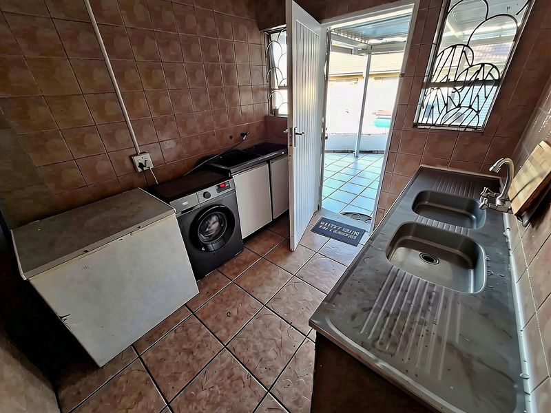 Functional laundry room featuring double stainless steel sink, tiled surfaces, and direct access to the outdoor patio area.
