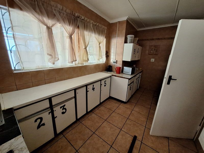 A dated kitchen featuring tiled flooring, wall-mounted cabinetry, and a large window with security bars, offering a functional layout ready for modernization.