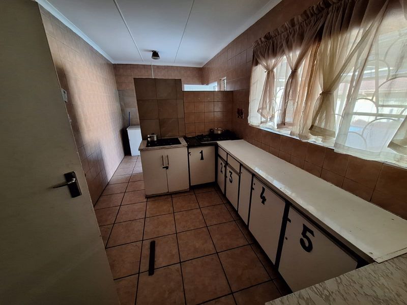 A dated kitchen featuring tiled walls and floors, built-in cabinetry with a cooktop, and ample counter space, offering potential for a modern renovation.