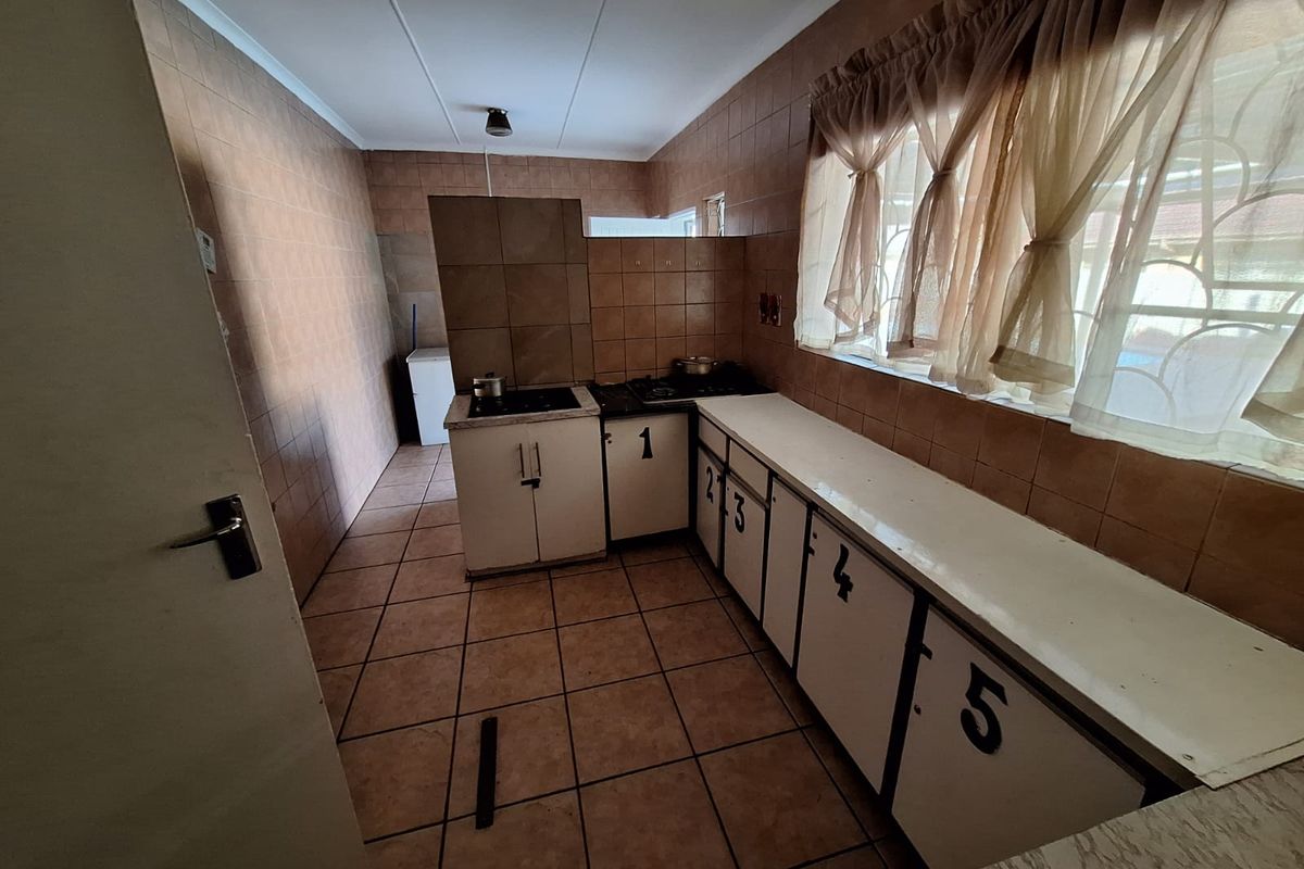 A dated kitchen featuring tiled walls and floors, built-in cabinetry with a cooktop, and ample counter space, offering potential for a modern renovation.