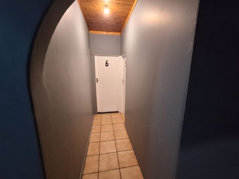 A narrow hallway featuring tiled flooring, a timber-paneled ceiling, and an arched entryway leading to a numbered door.
