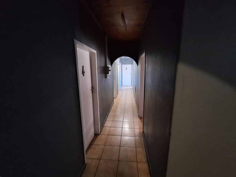 A long interior hallway featuring tiled flooring, a timber ceiling, and an arched transition, providing access to multiple rooms.
