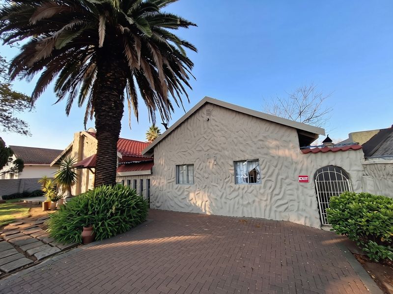 Front exterior view of the house featuring a brick paved driveway, textured facade, and tiled roof with established garden landscaping.