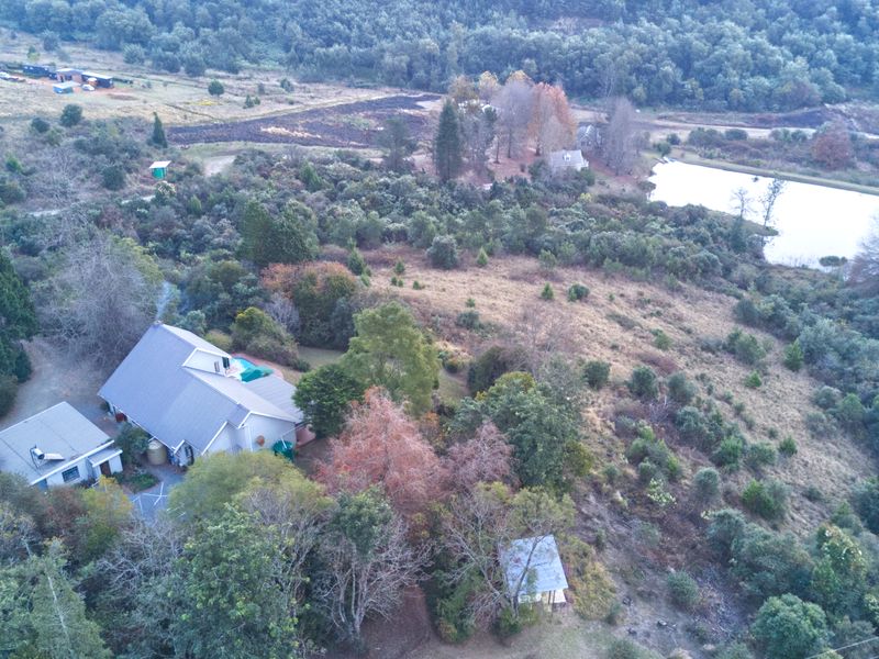 Aerial view of a small holding property featuring a main dwelling, outbuildings, a private dam, and extensive natural landscape.