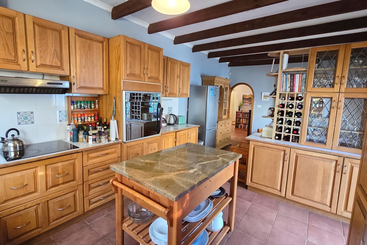 A traditional kitchen featuring extensive wooden cabinetry, exposed ceiling beams, stone countertops, and a central island, offering a warm and functional culinary space.