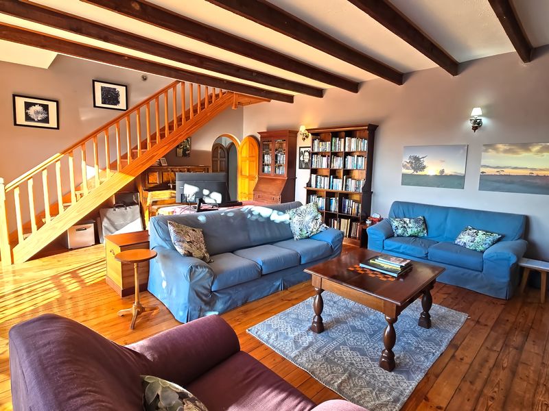 Spacious living room featuring warm timber flooring, exposed ceiling beams, and a prominent wooden staircase leading to the upper level.