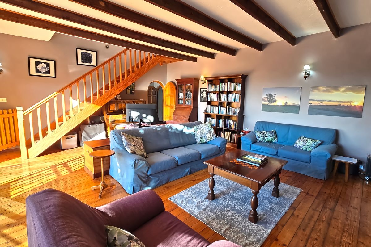 Spacious living room featuring warm timber flooring, exposed ceiling beams, and a prominent wooden staircase leading to the upper level.