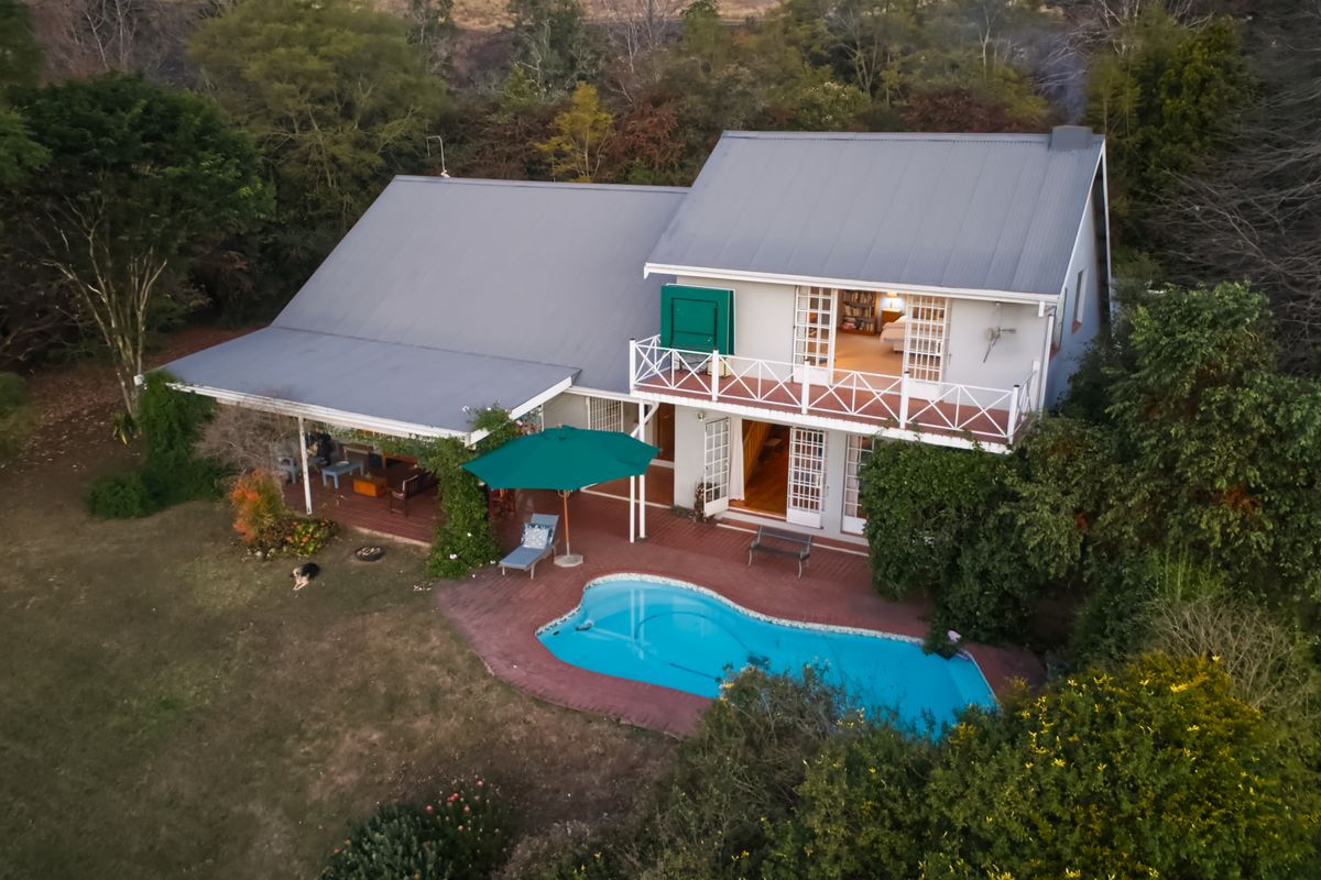 Aerial view of a two-story home featuring a swimming pool, covered patio, and balcony, set within a lush, tree-lined garden environment.