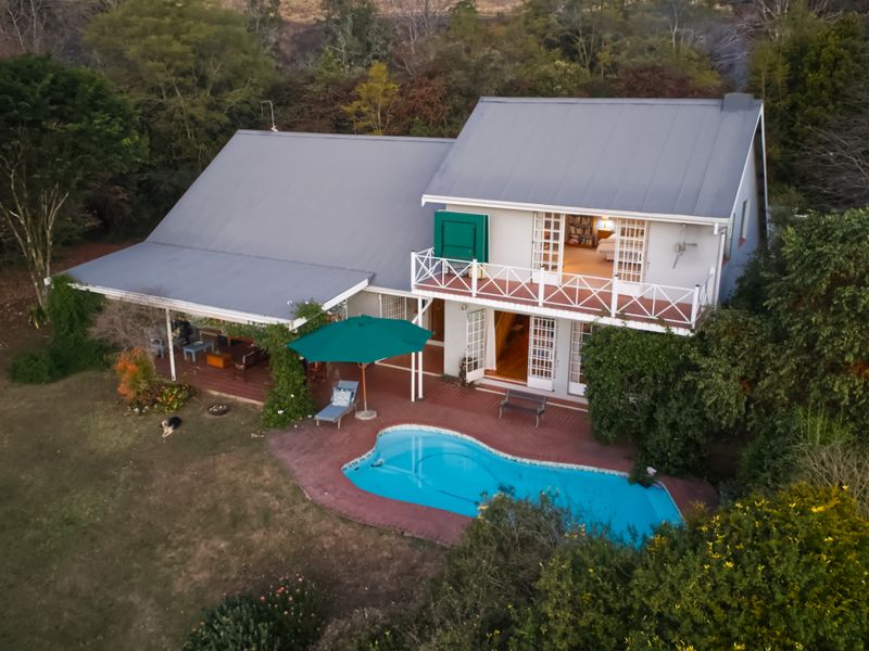 Aerial view of a two-story home featuring a swimming pool, covered patio, and balcony, set within a lush, tree-lined garden environment.