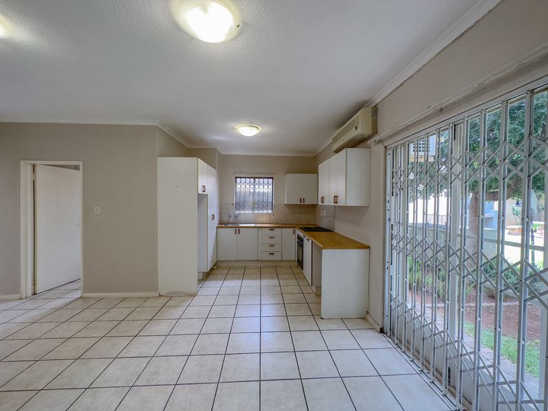 Open plan kitchen and living area featuring tiled flooring, built-in cabinetry, integrated appliances, and sliding glass doors with security gates leading to the exterior.