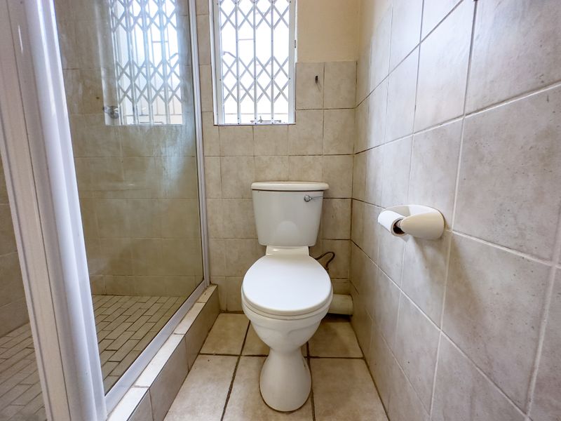 A compact bathroom featuring a standard toilet, a shower enclosure with glass door, and tiled walls and flooring throughout.