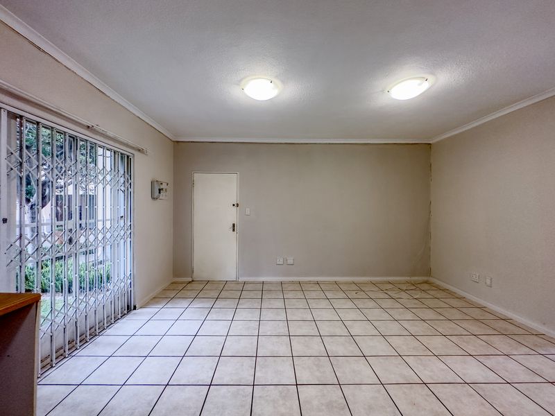 An empty living room featuring tiled flooring, a security gate, and a sliding door leading to the exterior.