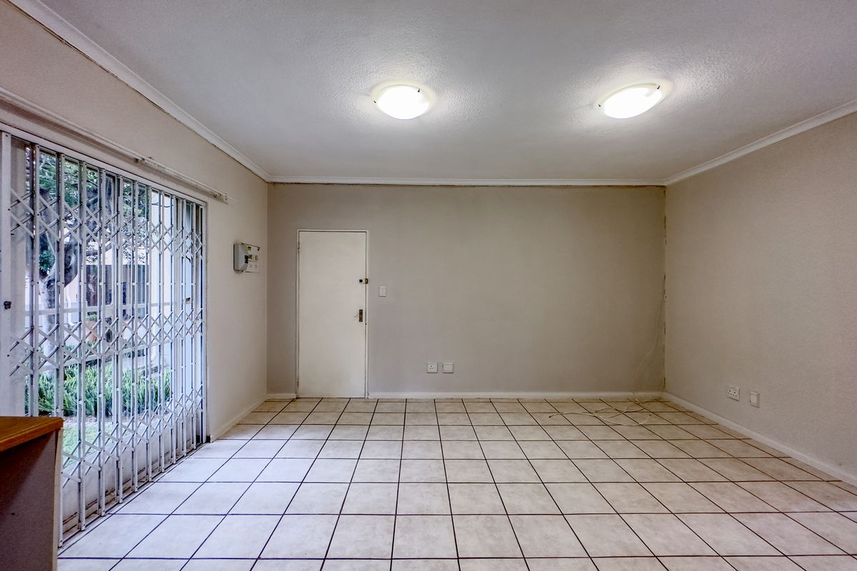 An empty living room featuring tiled flooring, a security gate, and a sliding door leading to the exterior.
