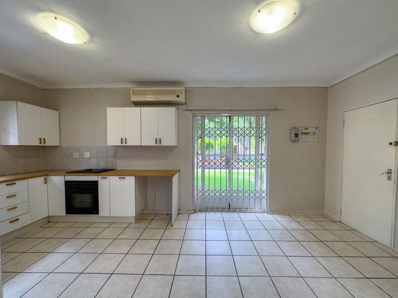 Open-plan kitchen and living area featuring tiled floors, built-in cabinetry with oven and hob, and a sliding door leading to an outdoor space.