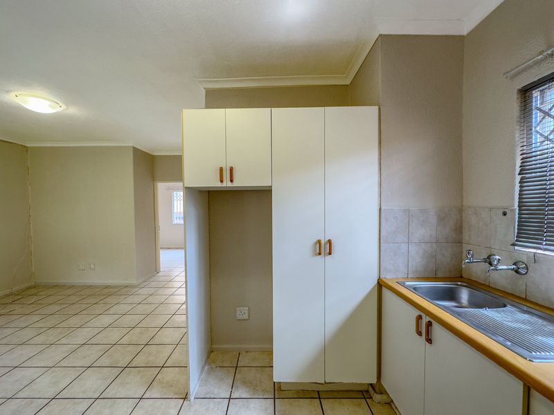 A functional, empty kitchen area featuring built-in white cabinetry, a stainless steel sink, and tiled flooring, leading into an open-plan living space.