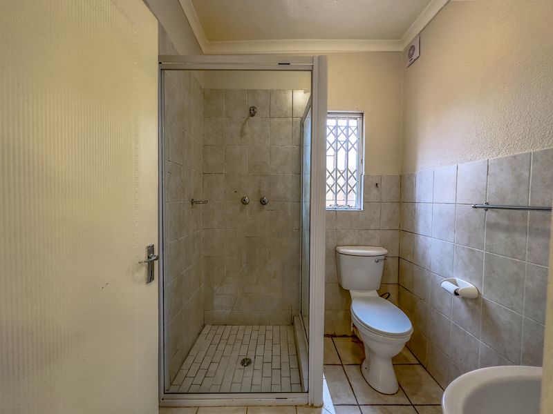 A functional bathroom featuring a glass-enclosed shower, toilet, and tiled finishes, offering a blank canvas for potential modernization and aesthetic updates.