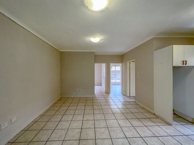 An empty open-plan living and kitchen area featuring tiled flooring, neutral walls, and built-in cabinetry, offering a blank canvas for renovation.