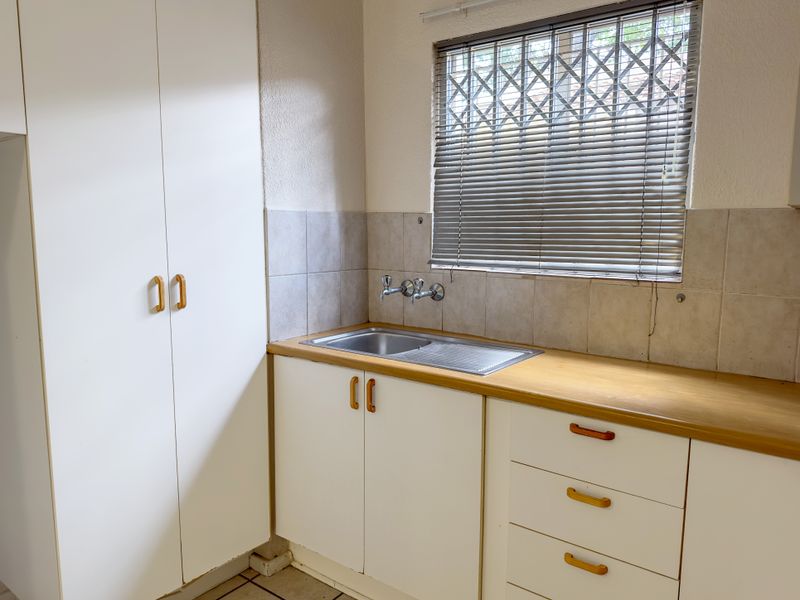 A functional laundry area featuring built-in cabinetry, a stainless steel sink, and a window with security bars.