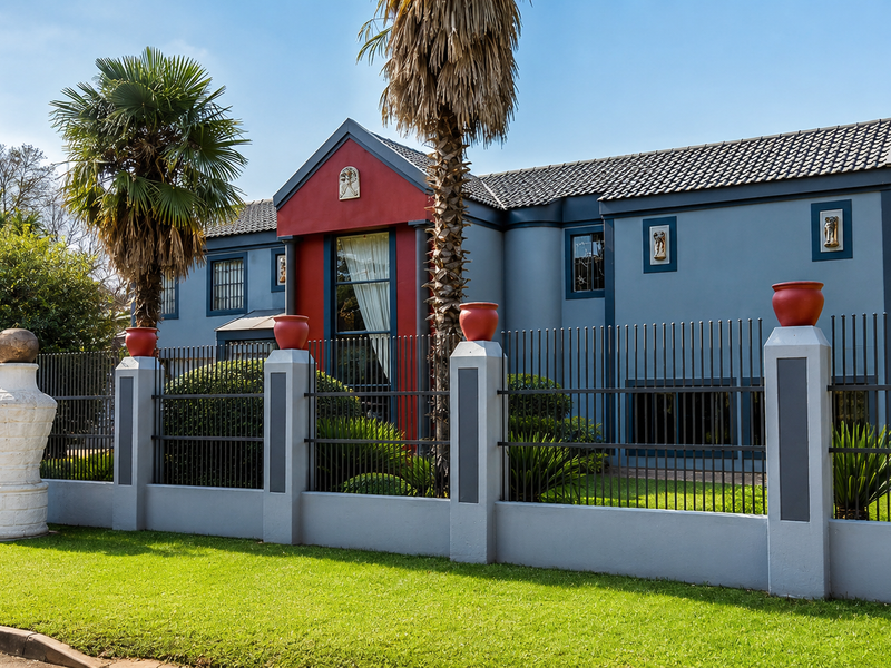 Front elevation of a two-story residence featuring a distinctive blue and red facade, secured by a modern wrought iron and masonry boundary fence.