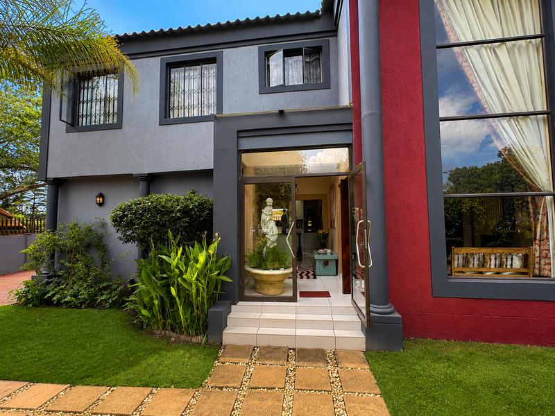 A well-maintained front entrance featuring a modern glass door, tiled steps, and a paved walkway set against a landscaped garden.