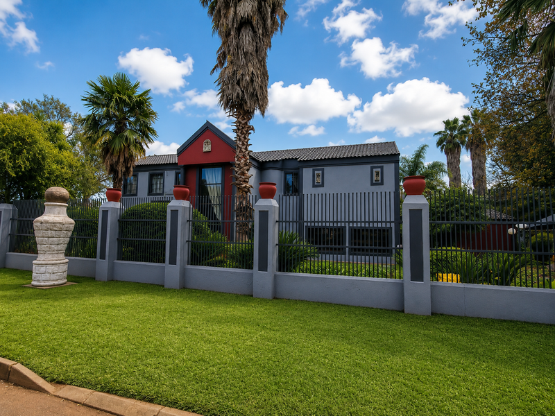 Front view of a two-story house featuring a modern plastered facade, tiled roof, and secure metal perimeter fencing with a landscaped front lawn.