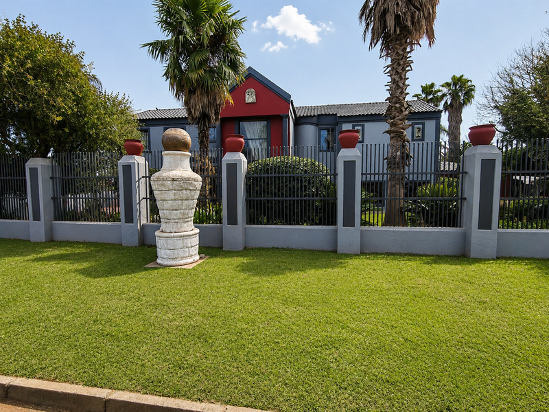Front view of a residential property featuring a well-maintained lawn, perimeter fencing with concrete pillars, and a multi-toned exterior facade.