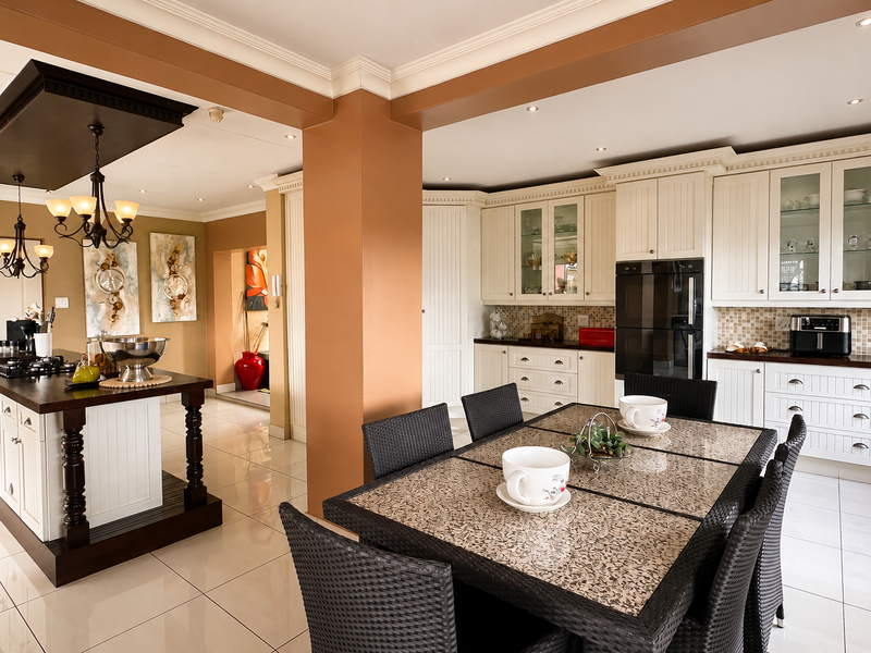 Spacious open-plan kitchen and dining area featuring a large central island, classic white cabinetry, built-in appliances, and polished tile flooring throughout.