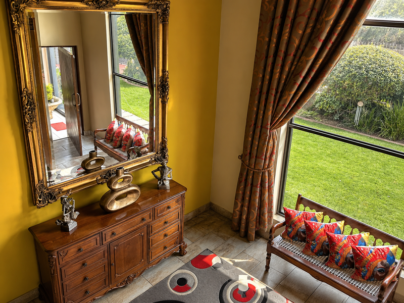 A bright entrance area featuring large windows with garden views, tiled flooring, and a warm yellow wall finish.