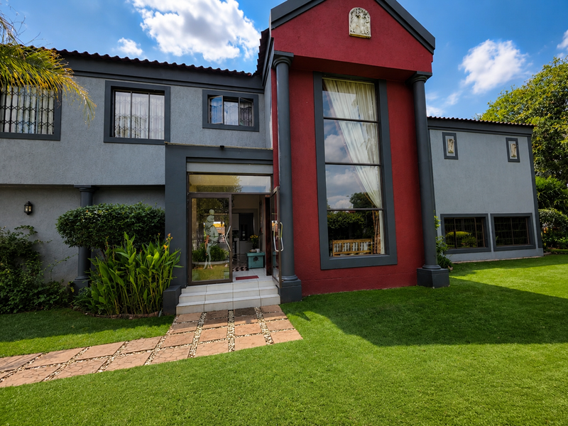 Front elevation of a two-story residence featuring a striking red facade, double-height window, decorative columns, and a paved walkway leading to the entrance.
