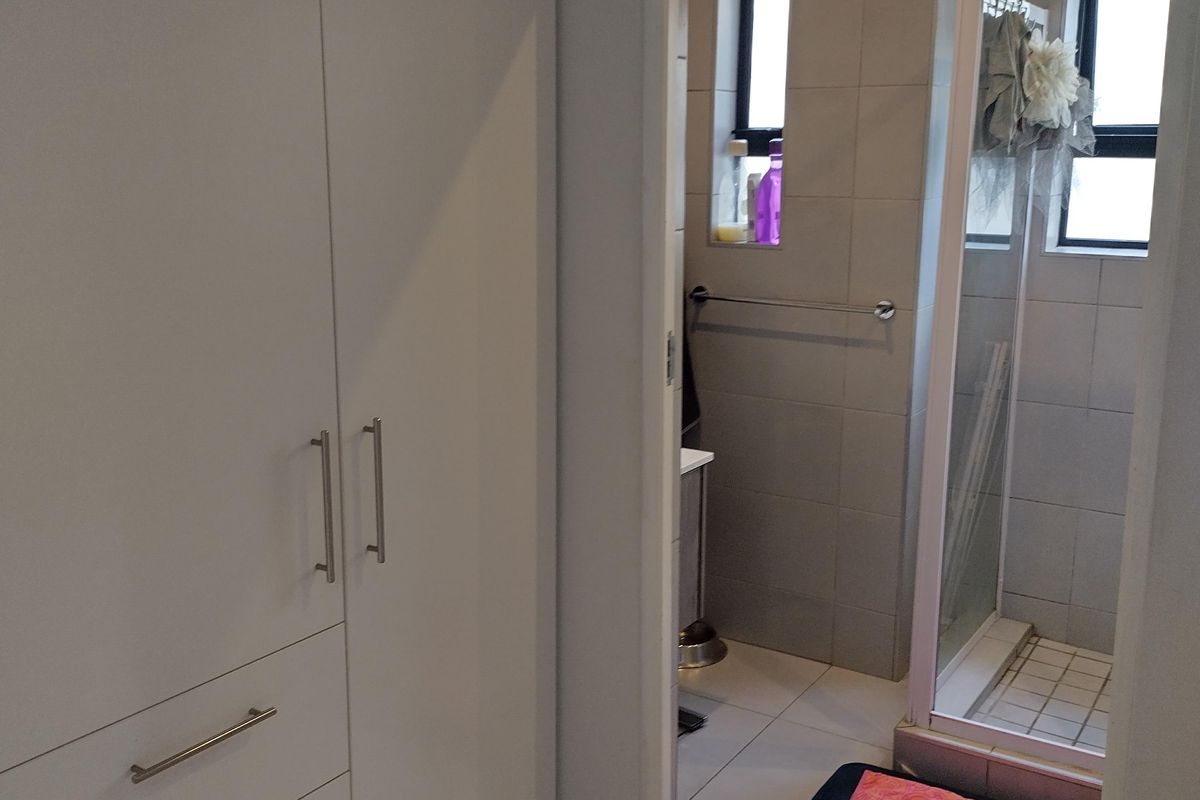 A functional bathroom featuring a shower enclosure, tiled finishes, and adjacent built-in storage cupboards.