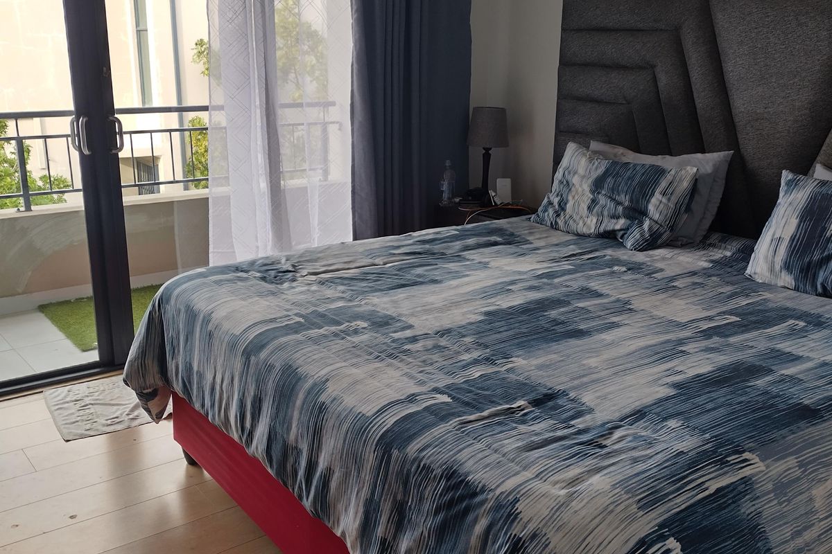 A well-lit bedroom featuring laminate flooring and a large sliding glass door providing direct access to an outdoor balcony.