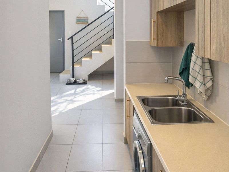 A modern, well-maintained laundry area featuring built-in cabinetry, a stainless steel sink, and tiled flooring, leading towards an internal staircase.