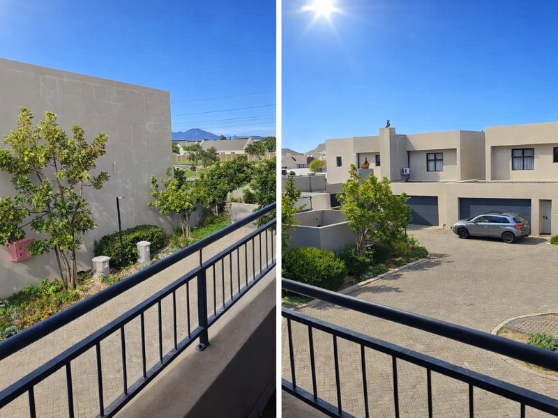 View from an elevated balcony overlooking a paved driveway, garage entrances, and landscaped garden area of a modern residential property.