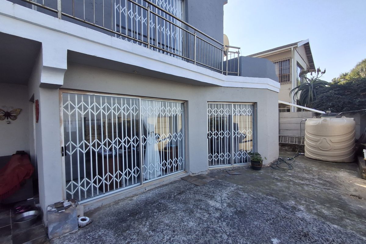 Rear exterior view featuring a concrete patio, sliding glass doors with security gates, and an upper-level balcony with metal railings.