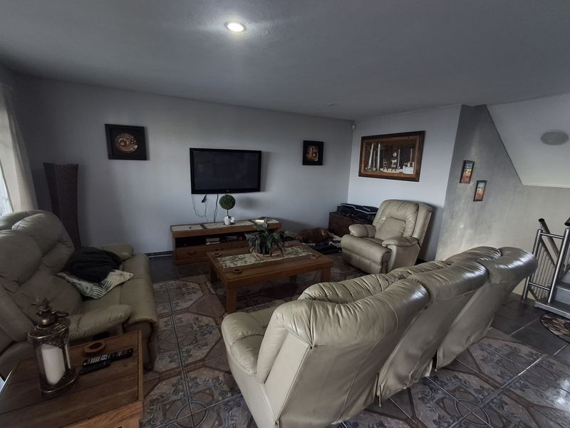 A comfortable living room featuring tiled flooring, recessed ceiling lighting, and a staircase leading to the upper level.