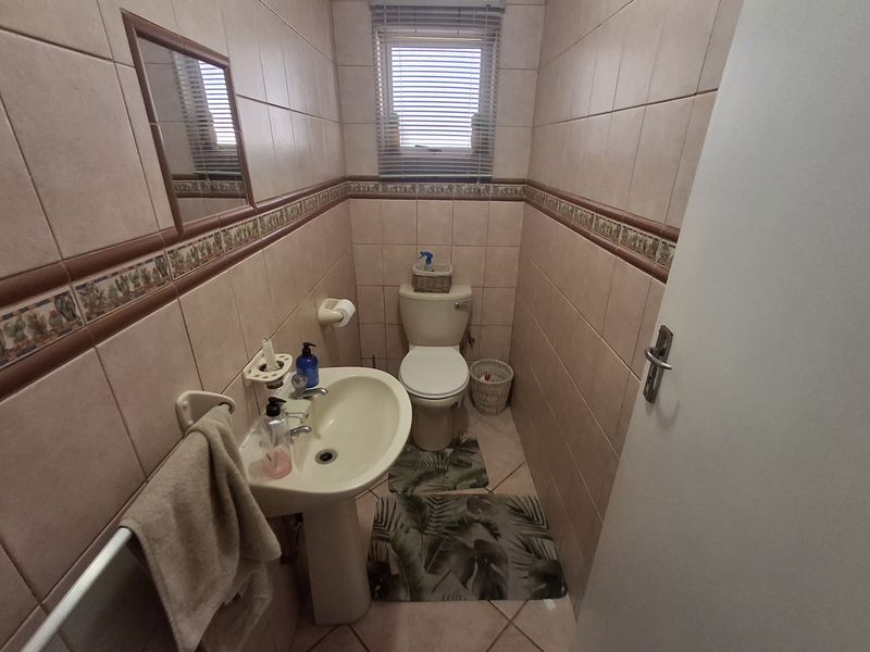 A compact guest bathroom featuring a pedestal basin, toilet, and full-height wall tiling with a decorative border.