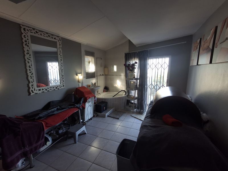 A functional bathroom space currently utilized as a treatment room, featuring a corner bathtub, pedestal basin, and direct access to an outdoor area.