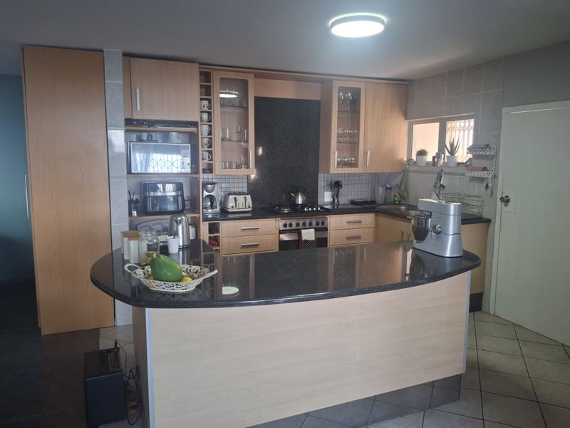 Functional kitchen featuring light wood cabinetry, dark granite countertops, a breakfast bar, and integrated cooking appliances.