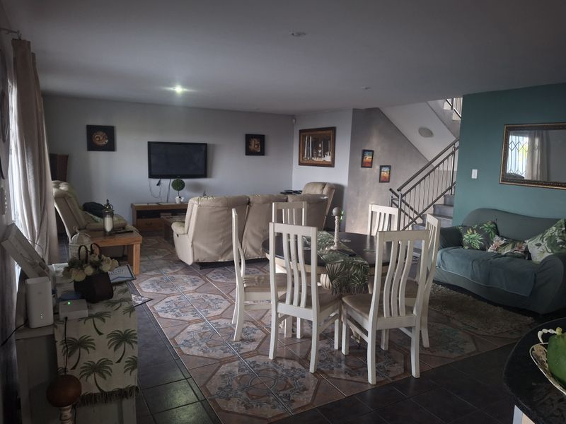 Spacious open-plan living and dining area featuring decorative tiled flooring, a staircase with metal balustrade, and a vibrant teal accent wall.