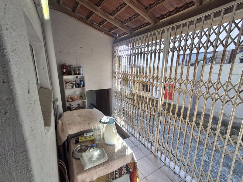 A covered outdoor patio area featuring tiled flooring, exposed timber rafters, and a metal security gate, suitable for a utility or laundry space.