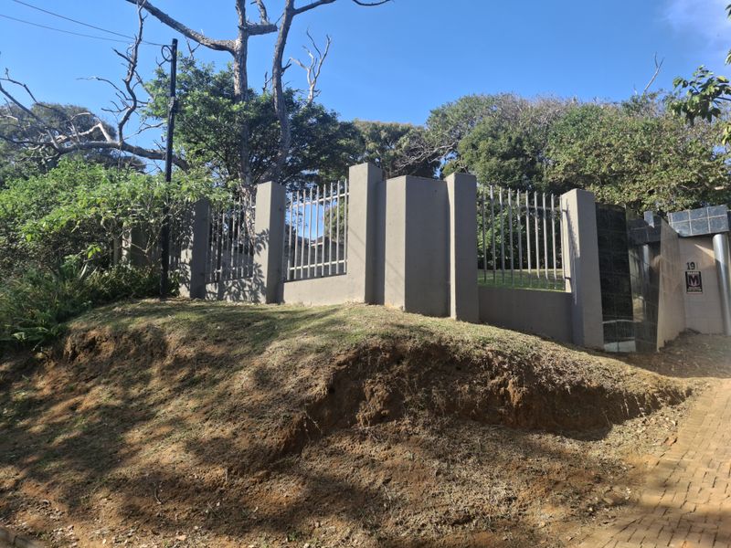 Front view of the property featuring a solid concrete boundary wall with integrated metal security fencing and a paved entrance area.